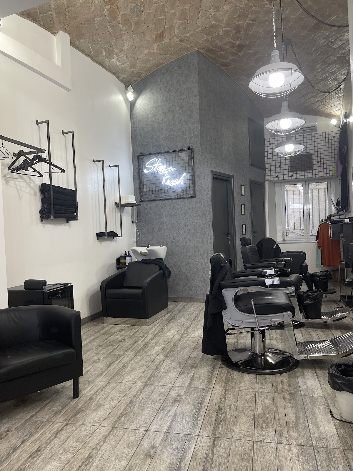 Interno di Fresh Barbershop Prati: poltrone da barbiere e soffitto a volta in mattoni con insegna al neon